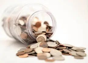 a jar full of coins with silver coins spilling out shows investors' move towards hedging assets such as physical silver and physical gold