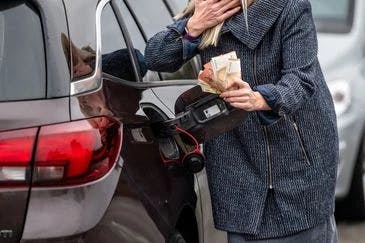 Die hohe Inflation und die steigenden Benzinpreise werden in einem Bild mit einer Frau dargestellt, die tankt und Euro-Scheine in der Hand hält.